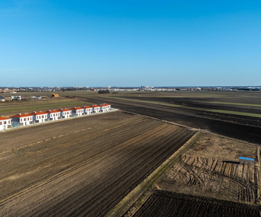 Szereg białych domów na środku pustego pola w Ożarowie Mazowieckim. O planach ogólnych przeczytasz na Muratordom.