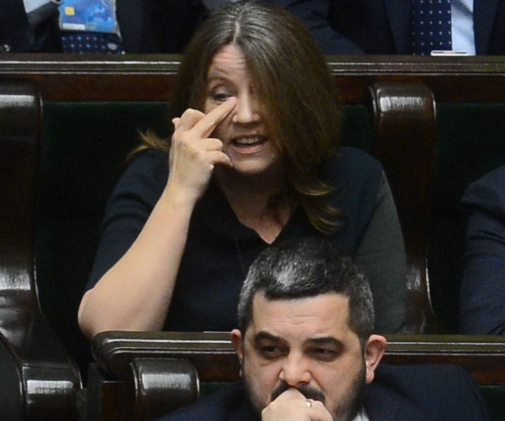 Posłanka Joanna Lichocka podczas obrad w Sejmie, poprawiająca włosy lub przecierająca oko, w tle widać innego polityka. Więcej o jej aktywności politycznej i oświadczeniu majątkowym przeczytasz na naszym portalu.