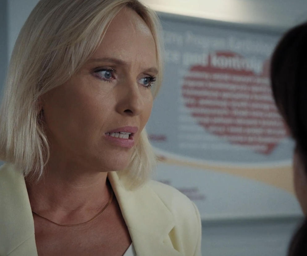 Iwona Rejzner jako Dorota z M jak miłość w jasnej marynarce, zaniepokojona rozmową w szpitalu. Blada cera, lekko rozchylone usta, skupione spojrzenie wyrażające niepokój. Artykuły o serialach takich jak M jak miłość znajdziesz na Super Seriale.