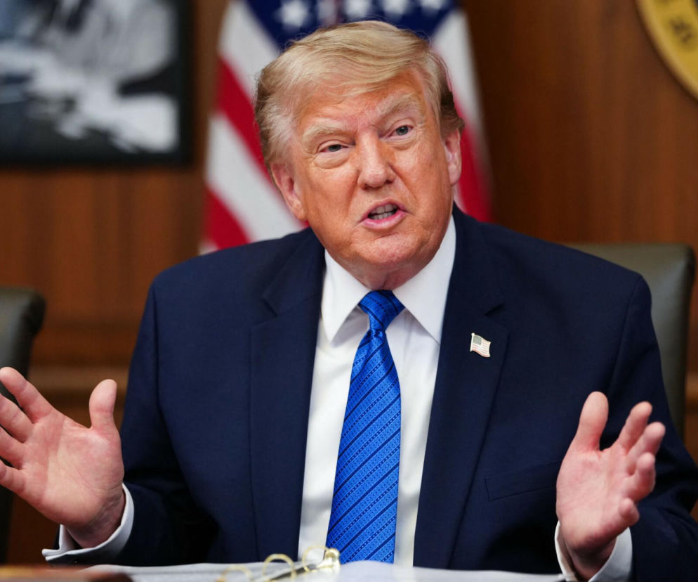 Donald Trump przemawia, gestykulując dłońmi. W tle flaga USA. O pamięci o Powstaniu Warszawskim przeczytasz w Eska.