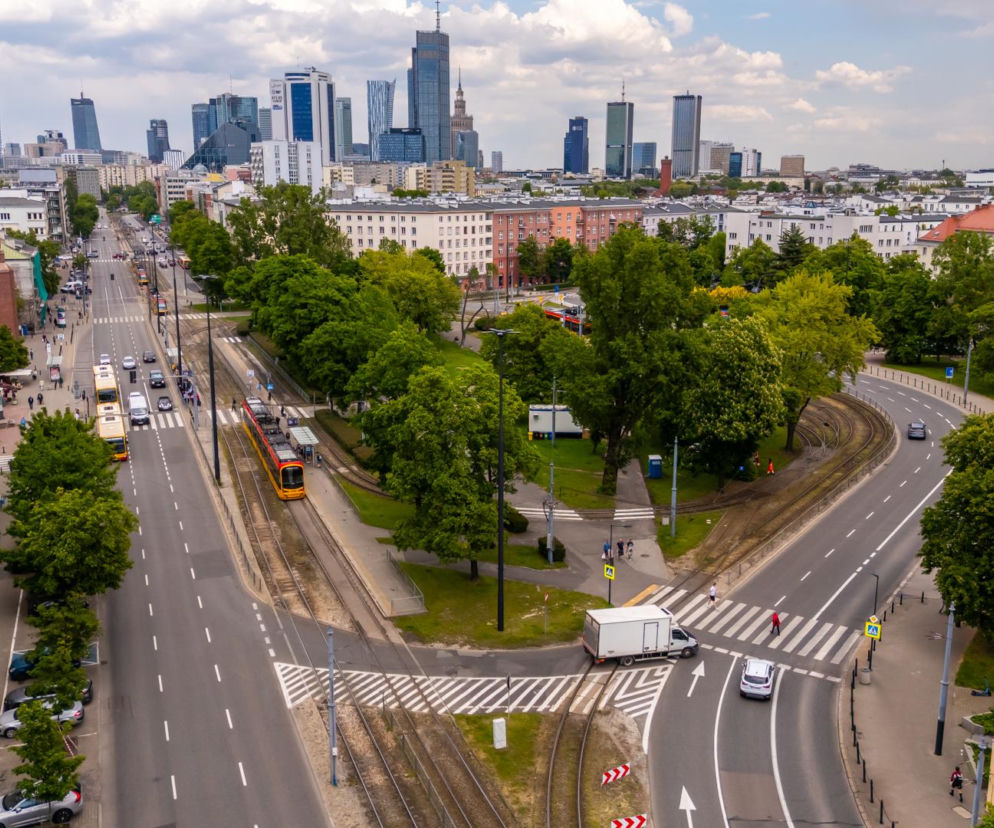 Ulica Grójecka w Warszawie, widziana z góry, z ruchem samochodowym i tramwajowym. W tle panorama miasta z wieżowcami, a na pierwszym planie zabytkowy budynek z czerwonej cegły i zielone drzewa. O zmianach komunikacyjnych w stolicy przeczytasz na Architektura Murator Plus.