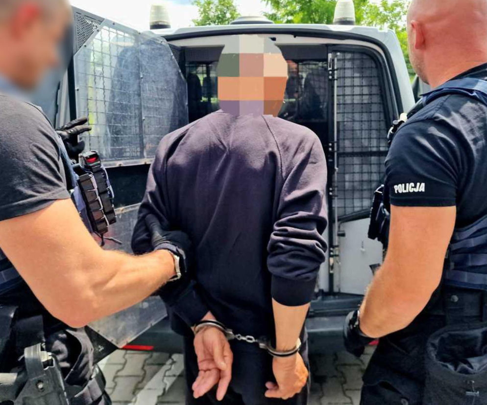 Dwaj policjanci wprowadzają mężczyznę w kajdankach do radiowozu. O zbrodni w Kaliszu przeczytasz na SE.