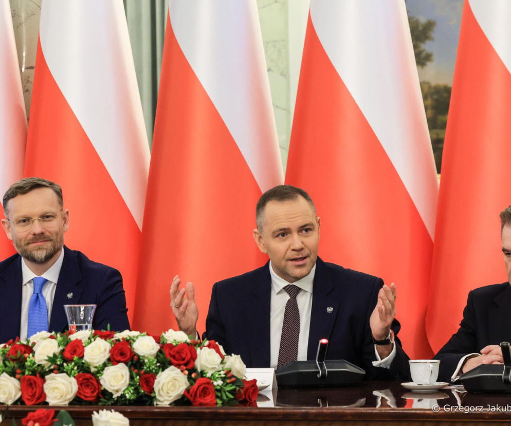 Trzech mężczyzn, w tym prezydent Karol Nawrocki (w środku), przewodniczący Solidarności Piotr Duda (po prawej) i polityk (po lewej), siedzi za stołem konferencyjnym z mikrofonami i bukietami róż na tle polskich flag, podczas spotkania dotyczącego emerytur, o czym możesz przeczytać na Super Biznes.