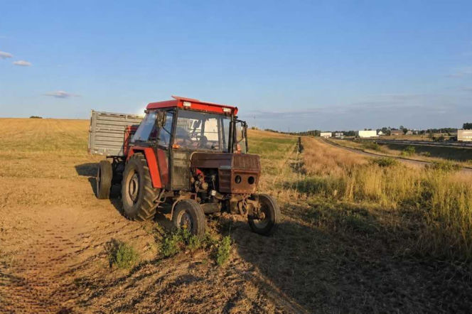 Czerwony ciągnik rolniczy z przyczepą stoi na poboczu pola przy drodze. O pościgu w Myśliborzu przeczytasz na Eska Szczecin.