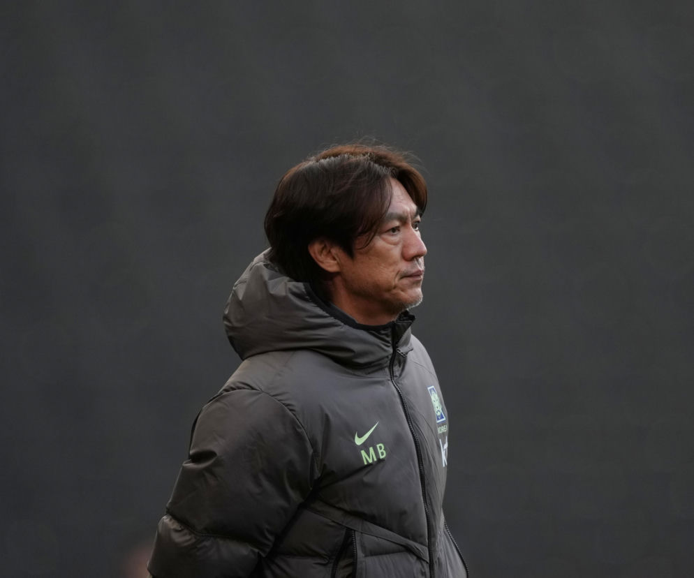 Hong Myung-bo, były selekcjoner reprezentacji Korei Południowej, ubrany w puchową kurtkę z logiem Nike i napisem KOREA oraz MB, patrzący w prawo z zamyślonym wyrazem twarzy na tle ciemnej ściany. Więcej o aferze przeczytasz na naszym portalu.