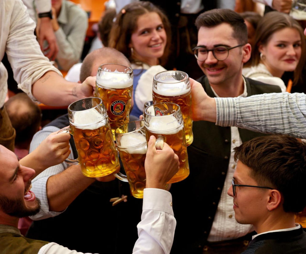 Grupa uśmiechniętych ludzi wznosi toast kuflami piwa. O pierwszym zgonie alkoholowym na Oktoberfest przeczytasz na SE.