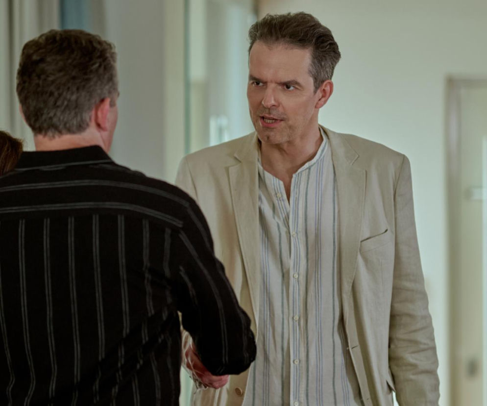 Ujęcie dwóch mężczyzn: Robert Jarociński (Sebastian) w beżowej marynarce i koszuli w paski rozmawia z Przemysławem Sadowskim (Lew Nalepa), który stoi tyłem w czarnej koszuli w paski. Zdjęcie ilustruje odcinek serialu Na Wspólnej, o czym przeczytasz więcej na Super Seriale.