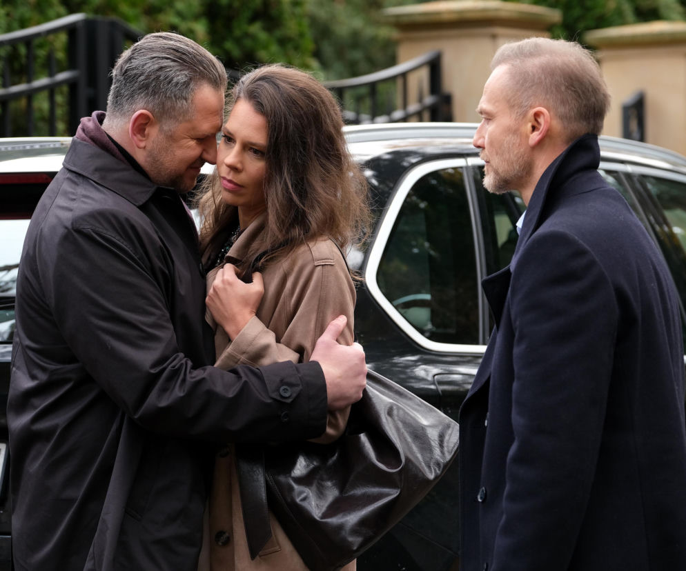 Krystian Wieczorek (Andrzej Budzyński) obejmuje Marię Wieczorek (Paulina Lipska) w dramatycznej scenie przed autem, obok stoi Marcin Piętowski (Igor Jabłoński). To stresujący moment z M jak miłość, odcinek 1918, dotyczący groźby kryminalisty. Więcej o losach bohaterów przeczytasz na Super Seriale.
