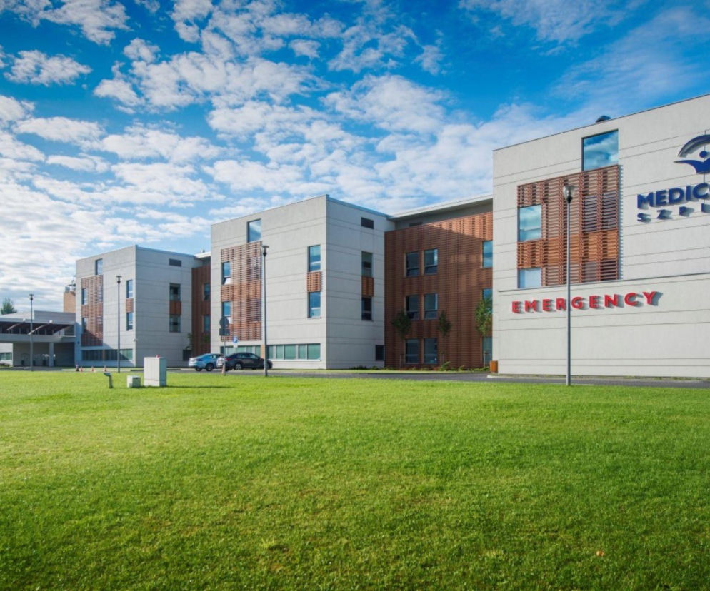 Nowoczesny budynek Szpitala Medicover w Warszawie z logo na fasadzie i napisem EMERGENCY na tle zielonego trawnika pod błękitnym niebem z chmurami. O rozwoju Kliniki Kardiologii w tym miejscu przeczytasz na naszym portalu.