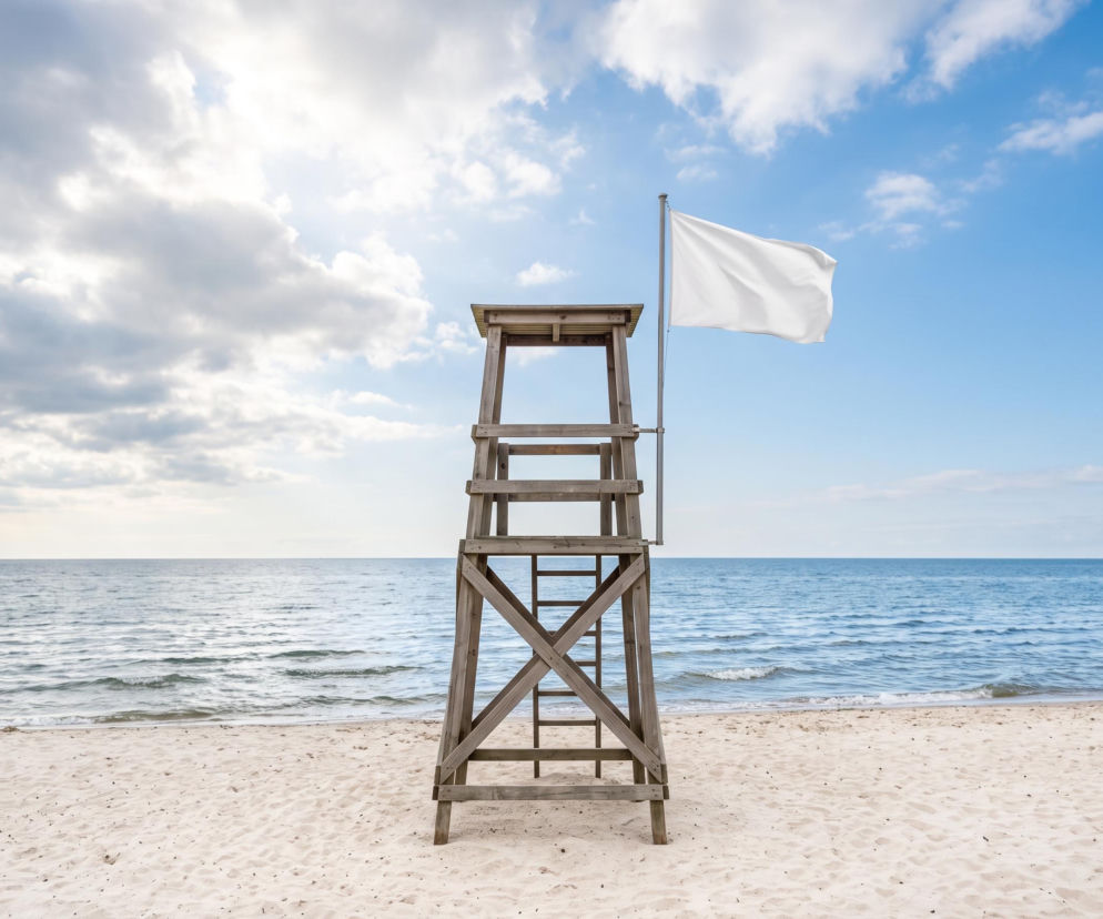 Drewniana wieża ratownika z białą flagą na plaży w Łazach. O czystej wodzie bez sinic przeczytasz na SE Szczecin.