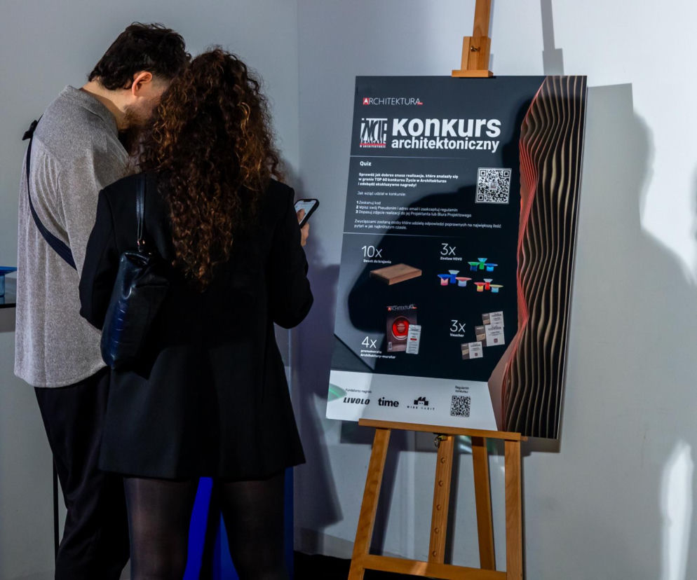 Dwóch uczestników finałowej gali 10. edycji konkursu „Życie w Architekturze” pochylonych nad tablicą z quizem architektonicznym. Tablica na sztaludze przedstawia zasady quizu oraz listę nagród od sponsorów LIVOLO i WHISE HABIT. Więcej o wydarzeniu na Architektura Murator Plus.
