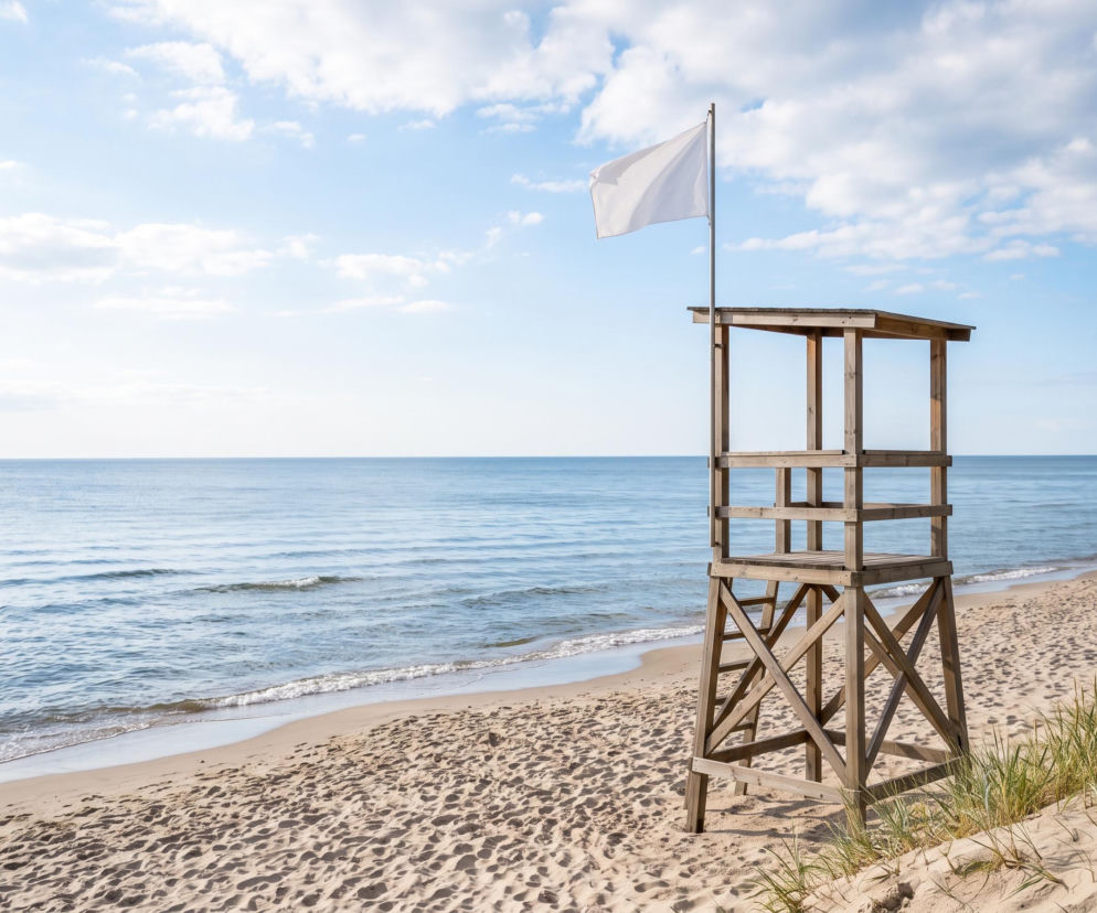 Drewniana wieża ratownicza z białą flagą na pustej plaży w Pobierowie. O braku sinic przeczytasz na SE Szczecin.