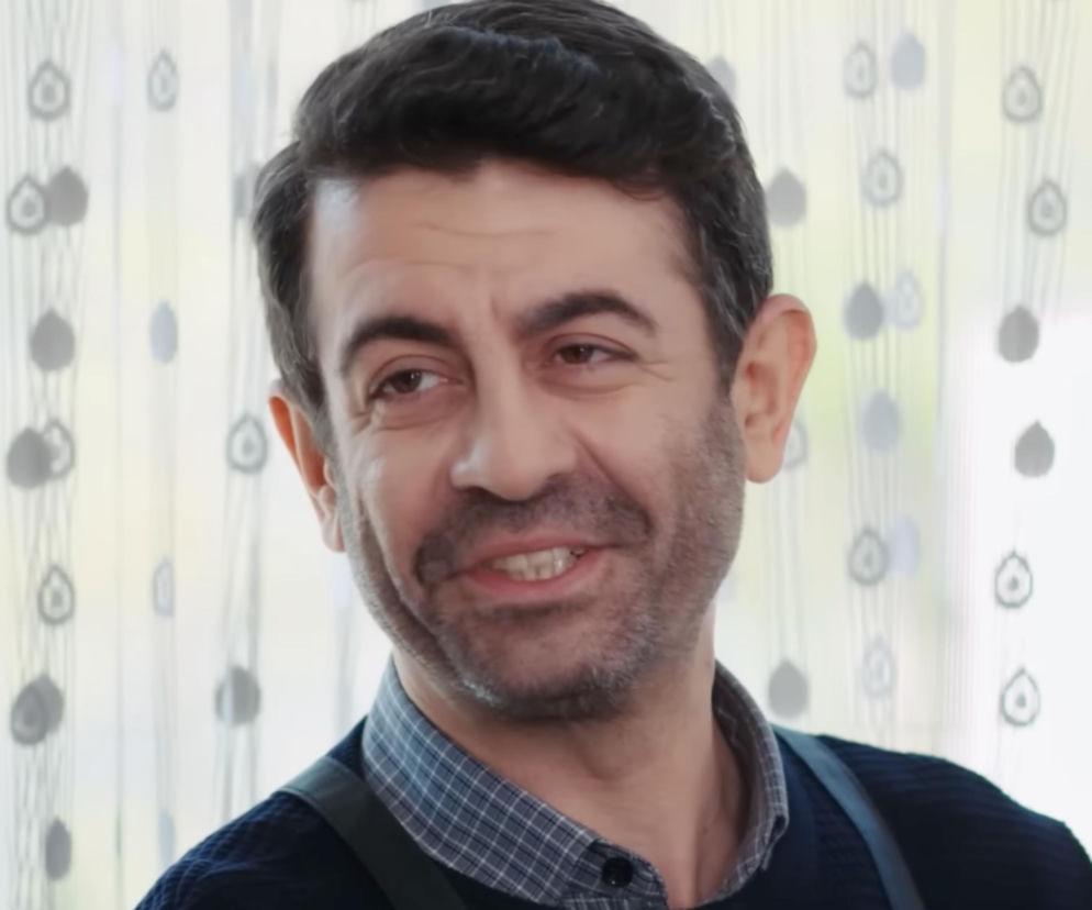 Cemil z serialu Panna młoda uśmiecha się na tle jasnej zasłony w kropki. O jego losach przeczytasz na SE Superseriale.