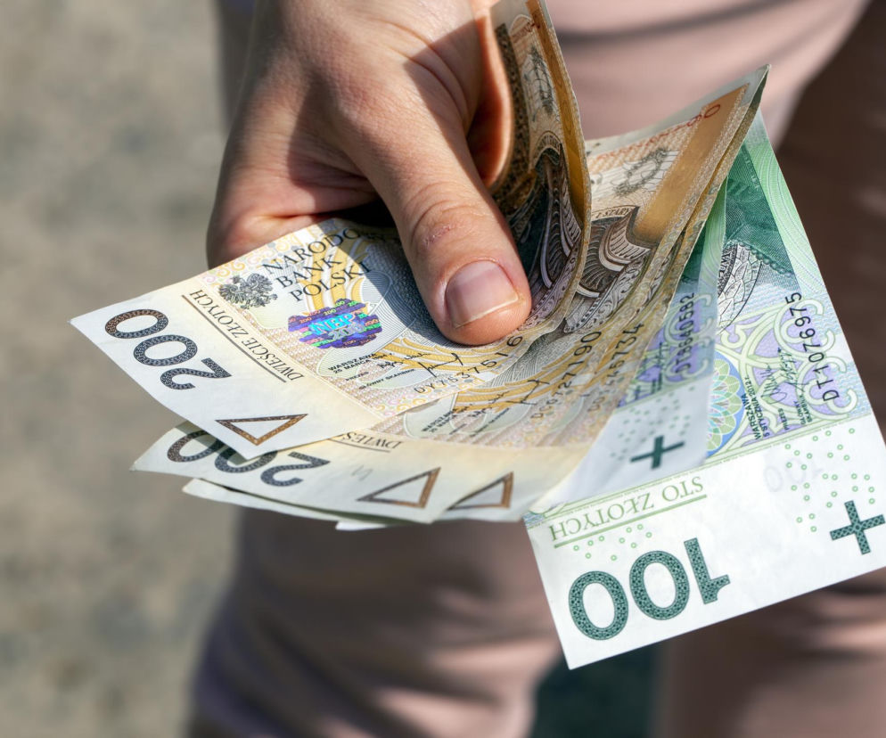 Dłoń osoby trzymającej banknoty o nominałach 200 i 100 złotych. O waloryzacji świadczeń przeczytasz w serwisie Eska.