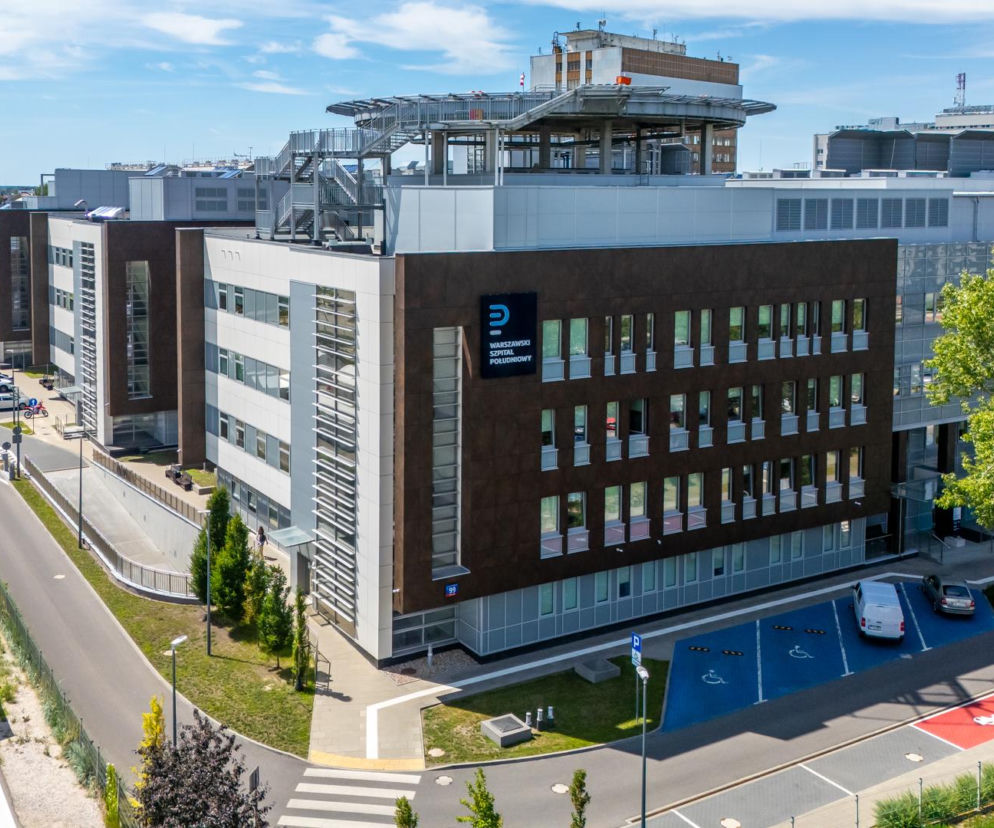 Budynek Warszawskiego Szpitala Południowego w Warszawie z lotu ptaka, ukazujący nowoczesną architekturę i otoczenie z zaparkowanymi samochodami, zielenią oraz namiotami medycznymi. Więcej informacji o szpitalu przeczytasz na naszym portalu.