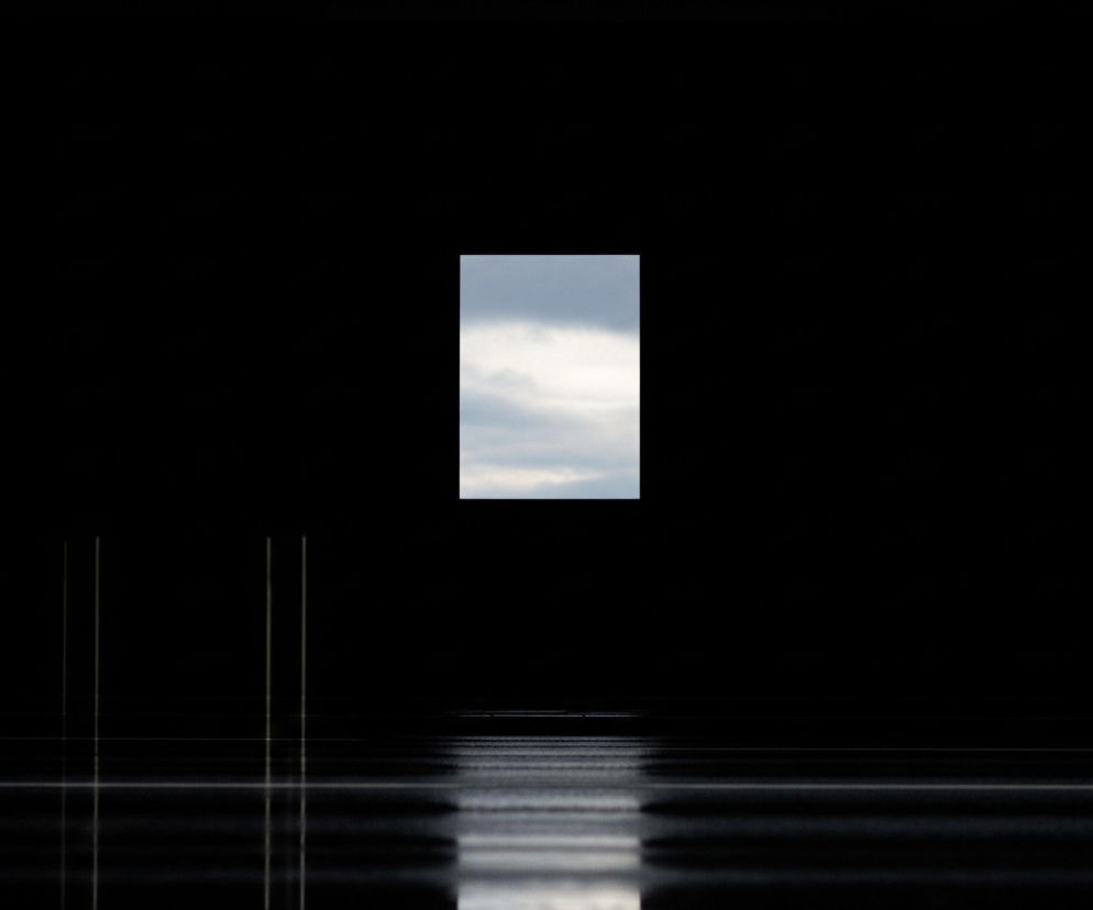 Ciemne tło z centralnie umieszczonym pionowym prostokątem wypełnionym niebem z chmurami w odcieniach błękitu i bieli. Poniżej prostokąta, na dole obrazu, widoczny jest odblask tej samej sceny, rozciągający się poziomo, z liniami i pasmami światła przypominającymi odbicie na tafli wody lub mokrej powierzchni. Po lewej stronie odbicia widoczne są dwie cienkie, pionowe, jasne linie, które również odbijają się w poziomej powierzchni.