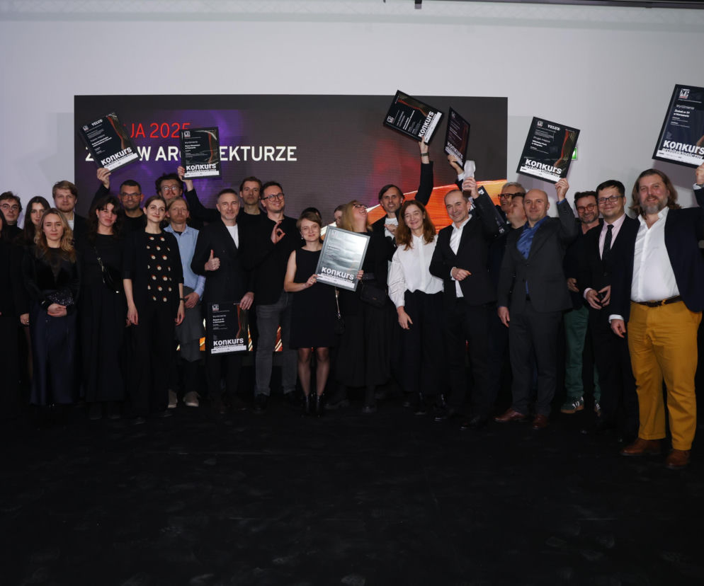 Grupa laureatów konkursu Życie w Architekturze 2025 z wyróżnieniami na scenie. Na zdjęciu widać kilkudziesięciu dorosłych ludzi, z których kilku unosi do góry pamiątkowe dyplomy. W tle widoczny jest duży ekran LED z napisem ŻYCIE W ARCHITEKTURZE. Artykuł o zwycięzcach można przeczytać na portalu Architektura Murator Plus.