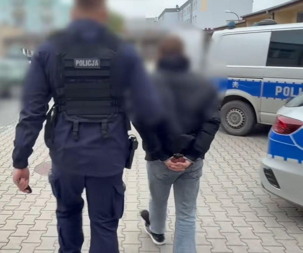 Policjant prowadzi zakutego w kajdanki mężczyznę do radiowozu. O zatrzymaniu sprawcy wypadku pisze SE Białystok.