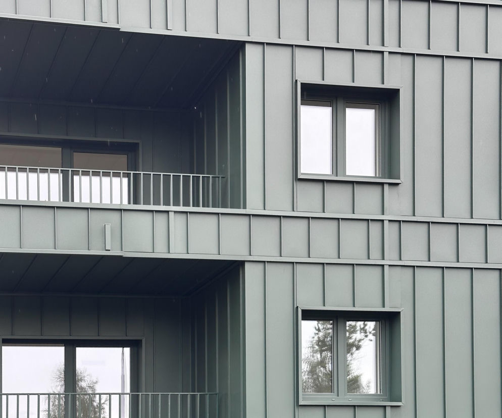 Zielona elewacja bloku z blachy trapezowej z oknami i balkonami. O nowym osiedlu TBS przeczytasz na Architektura.