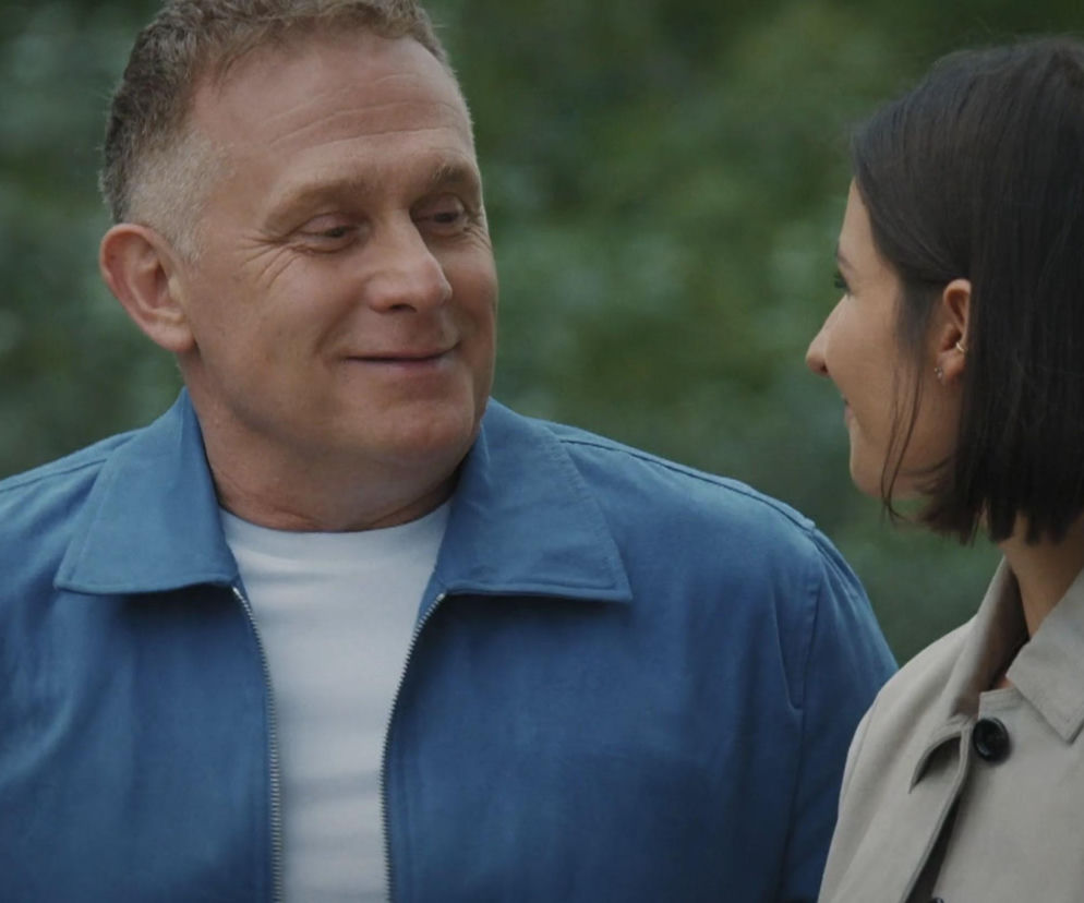 Uśmiechnięty Robert Moskwa (Artur Rogowski) w niebieskiej kurtce i Amanda Mincewicz (Agnes) w jasnym płaszczu rozmawiają z uśmiechem na twarzach w malowniczej scenerii, co zapowiada dramatyczne wydarzenia w M jak miłość. Więcej o serialu przeczytasz na Super Seriale.