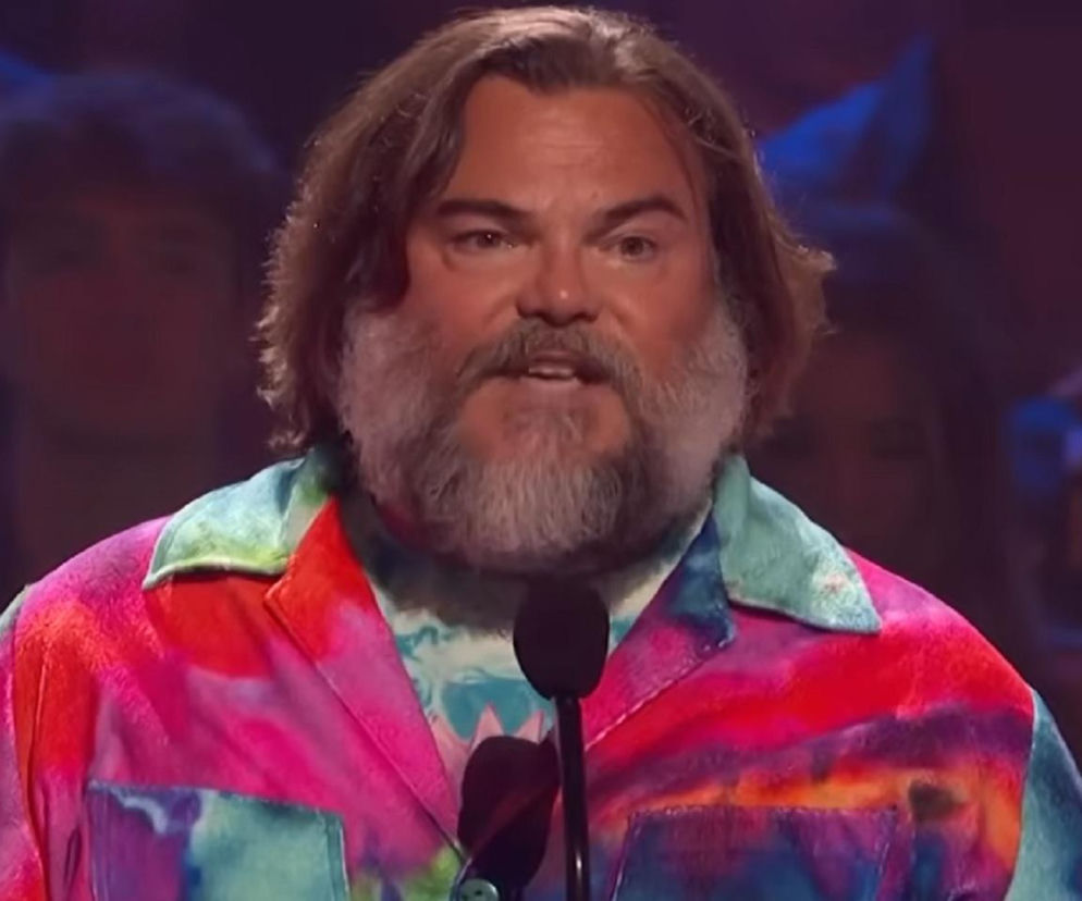 Aktor Jack Black w kolorowej koszuli tie-dye przemawia do mikrofonu. O opiniach na jego temat przeczytasz na EskaRock.