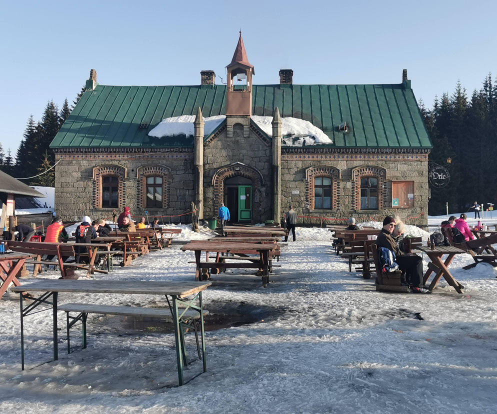 Kamienny budynek stacji Orle z drewnianymi ławami i turystami. O sporze wokół obiektu przeczytasz na Architektura.
