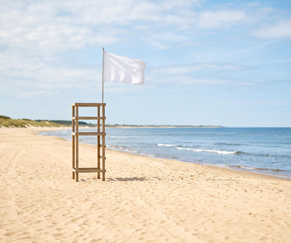 Biała flaga powiewa na wieży ratowniczej na pustej, piaszczystej plaży. O pogodzie w Świnoujściu przeczytasz na SE Szczecin.