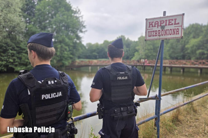 Policjanci przy tablicy kąpiel wzbroniona nad wodą. O bezpieczeństwie nad jeziorem przeczytasz na Radioplus.