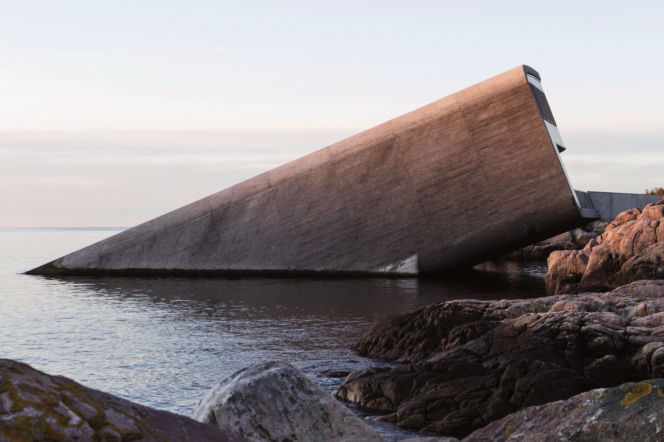 Monolityczna, betonowa bryła restauracji Under w Norwegii, nachylona pod kątem 20 stopni, częściowo zanurzona w Morzu Północnym. Widoczne skaliste wybrzeże o surowej estetyce. Więcej o tej niezwykłej architekturze znajdziesz na portalu Architektura Murator Plus.