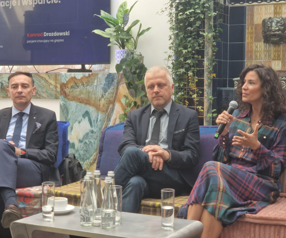 Trzy osoby podczas panelu dyskusyjnego o glejaku: mężczyzna w granatowym garniturze, Konrad Drozdowski pacjent z glejakiem oraz kobieta z mikrofonem w dłoni, siedzą na kanapach, przed nimi stolik z napojami. Temat artykułu o tym, że diagnoza glejaka nie musi oznaczać rezygnacji z życia. Więcej na ten temat znajdziesz na Poradnik Zdrowie.