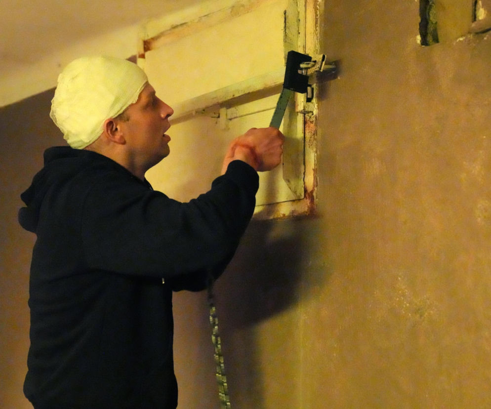 Łukasz Sadowski z Barw szczęścia z zabandażowaną głową i okrwawionymi rękami, ubrany w czarną bluzę, desperacko próbuje przeciąć kłódkę na okienku w więzieniu Agnieszki. Mężczyzna jest ledwo żywy po aresztowaniu byłej kochanki, o czym możesz przeczytać na Super Seriale.