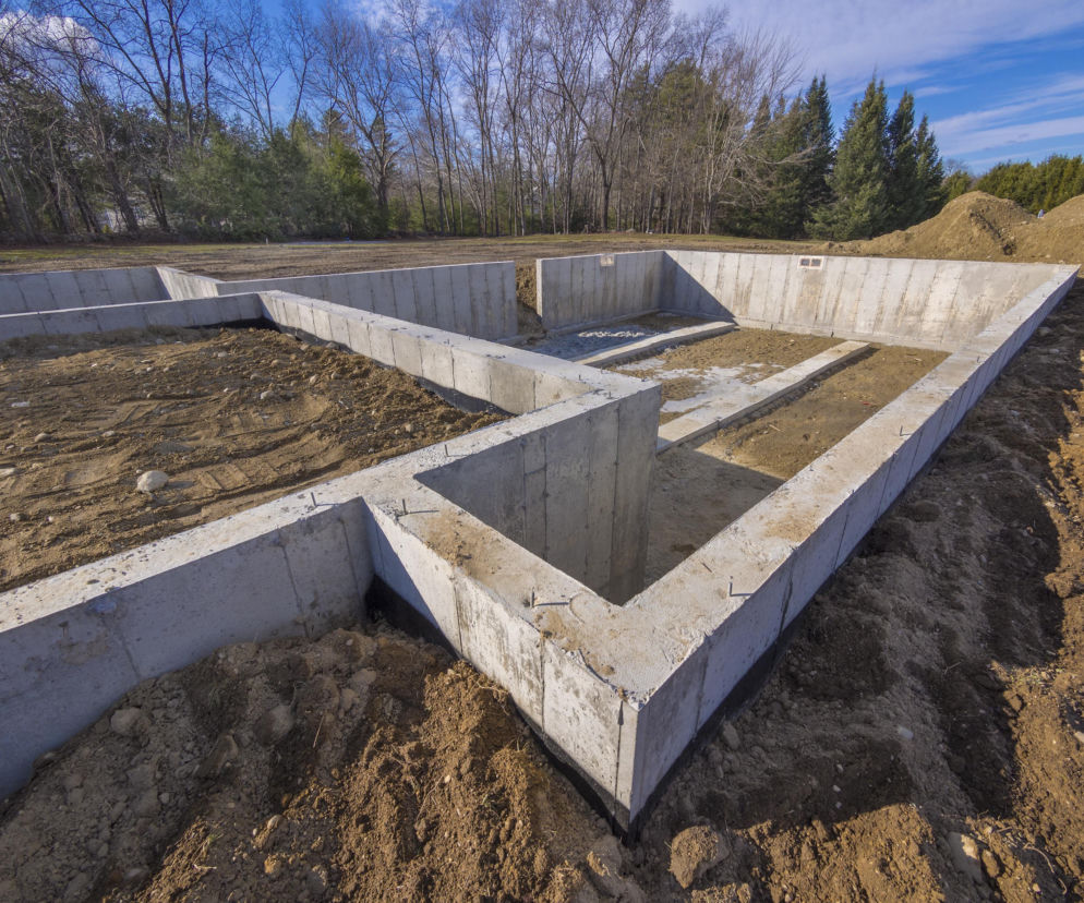 Betonowe fundamenty domu na pustej działce otoczonej lasem. O wygaśnięciu pozwolenia na budowę przeczytasz na Muratordom.