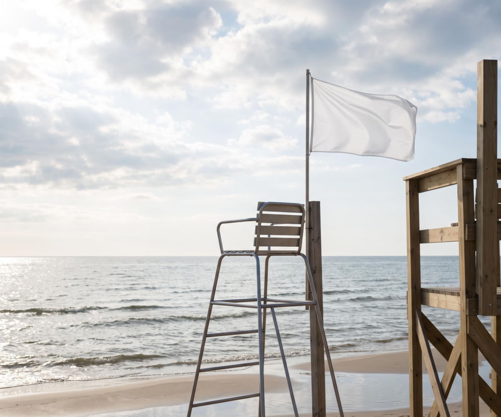 Biała flaga na plaży w Niechorzu obok stanowiska ratownika. O bezpieczeństwie kąpieli przeczytasz na SE Szczecin.