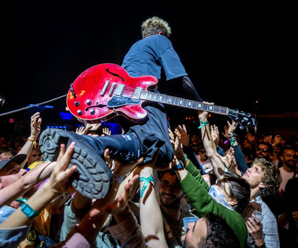 Artysta z czerwoną gitarą elektryczną uniesiony przez tłum fanów podczas koncertu na festiwalu Sziget. Dynamiczne ujęcie oddaje energię i atmosferę wydarzenia, o którym można przeczytać więcej na naszym portalu.