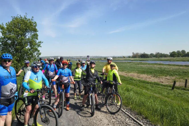 Grupa rowerzystów na ścieżce nad rzeką. O trasach rowerowych w Lubuskiem przeczytasz na Radioplus.