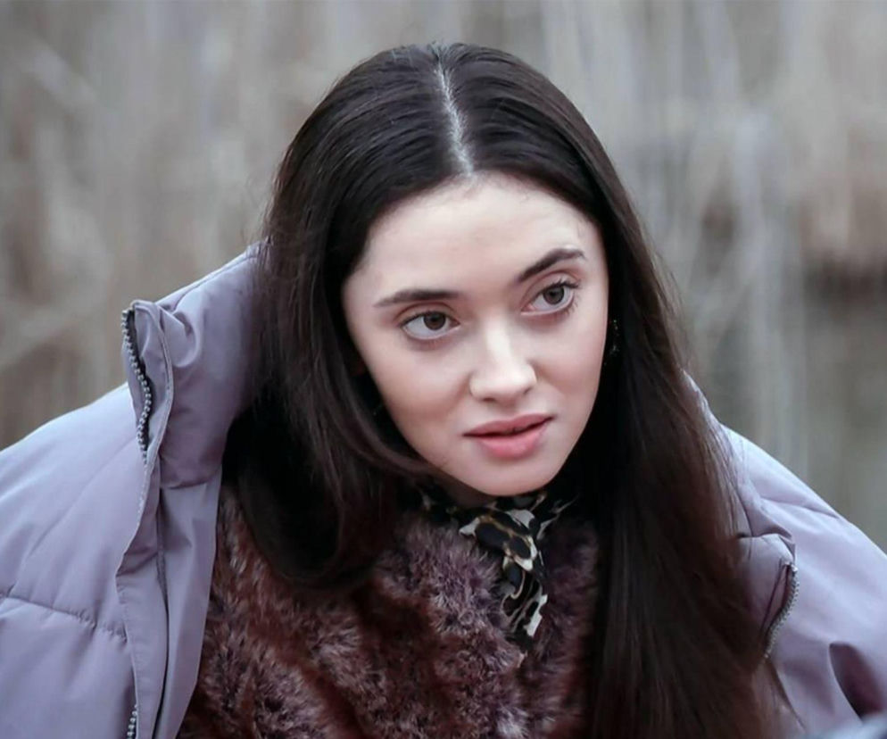 Kobieta z długimi, ciemnymi włosami w fioletowej puchowej kurtce i futerku, z zaniepokojoną miną, patrzy w bok. Scena prawdopodobnie przedstawia Angelikę z serialu Pierwsza miłość przed brutalnym porwaniem, o czym przeczytasz na Super Seriale.