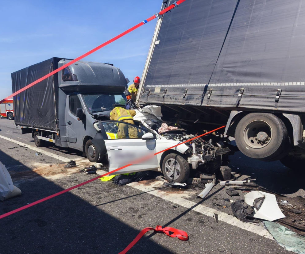 Karambol na autostradzie A1 w Dobieszowicach: dwa rozbite ciężarówki i biały samochód osobowy zniszczonym przodem, z uwięzionymi w środku ludźmi, wokół fragmenty pojazdów i krew. Służby ratunkowe pracują na miejscu, zabezpieczone czerwonymi taśmami. Więcej informacji znajdziesz na naszym portalu.