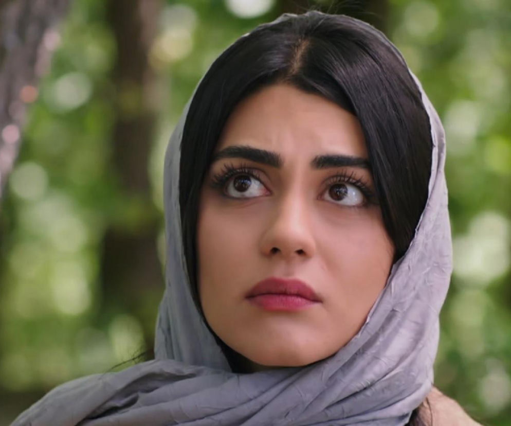 Hancer (Talya Celebi) w szarej chuście, z zaskoczonym wyrazem twarzy, patrzy w górę, słuchając Cihana. Kobieta ma długie czarne włosy i wyraźny makijaż, a w tle widać rozmazane zielone liście. Więcej o ich losach na Super Seriale.