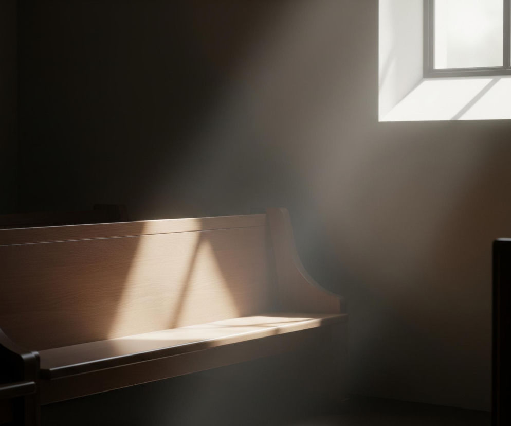 Drewniana ławka w jasnym odcieniu brązu zajmuje lewą i środkową część kadru, częściowo oświetlona silnym, jasnym promieniem światła padającym skośnie z góry. Promień światła tworzy widoczne smugi kurzu w powietrzu i rozświetla fragment oparcia oraz siedzisko ławki, podkreślając fakturę drewna. Po prawej stronie, w górnym rogu, widoczne jest prostokątne okno z ciemnymi, cienkimi ramami dzielącymi je na cztery szyby, przez które wpada intensywne, białe światło, rzucające cienie na ścianę poniżej. Większość pomieszczenia pozostaje w głębokim cieniu, tworząc kontrast między jasnością a ciemnością, a podłoga jest ciemna i jednolita.