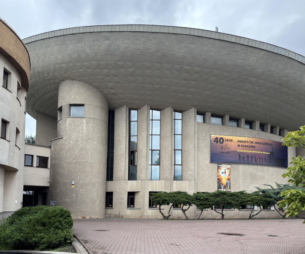 Kościół św. Jana Kantego w Krakowie, budynek o futurystycznym kształcie, przypominający spodek UFO, z charakterystycznymi pionowymi oknami i zaokrąglonymi ścianami. Na fasadzie wisi baner informujący o 40-leciu parafii, o czym można przeczytać na Architektura Murator Plus.
