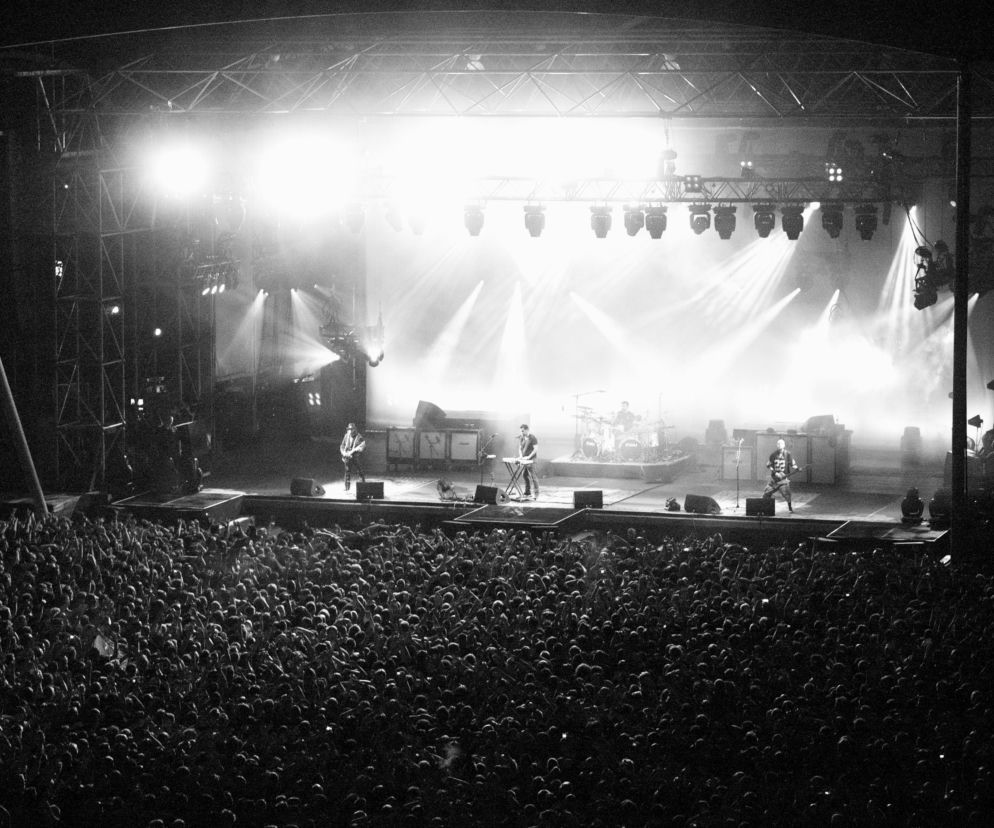 Czarno-białe zdjęcie koncertu System Of A Down. Tłum fanów pod oświetloną sceną. O wydarzeniu przeczytasz na EskaRock.