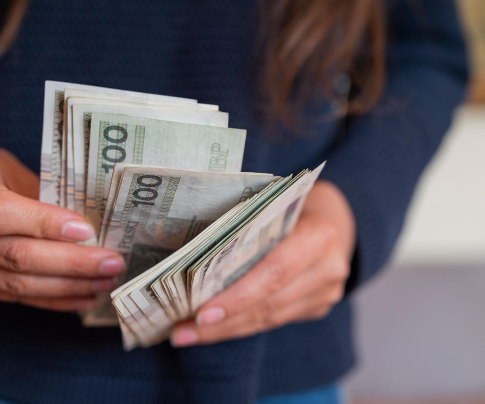 Dłonie osoby przeliczającej plik banknotów o nominale 100 złotych. O sankcji kredytu darmowego przeczytasz na SE.