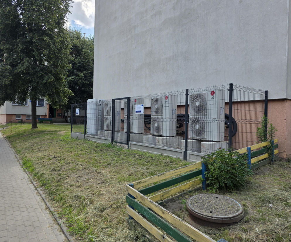 Rząd pomp ciepła za ogrodzeniem przy bloku mieszkalnym. O transformacji energetycznej miast przeczytasz na SE.