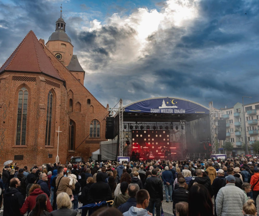 Tłum ludzi zgromadzony przed sceną z napisem Dobry Wieczór Gorzów podczas wydarzenia plenerowego, obok gotycki kościół, a nad całością burzowe niebo. Więcej o kulturalnym weekendzie w Gorzowie przeczytasz na naszym portalu.