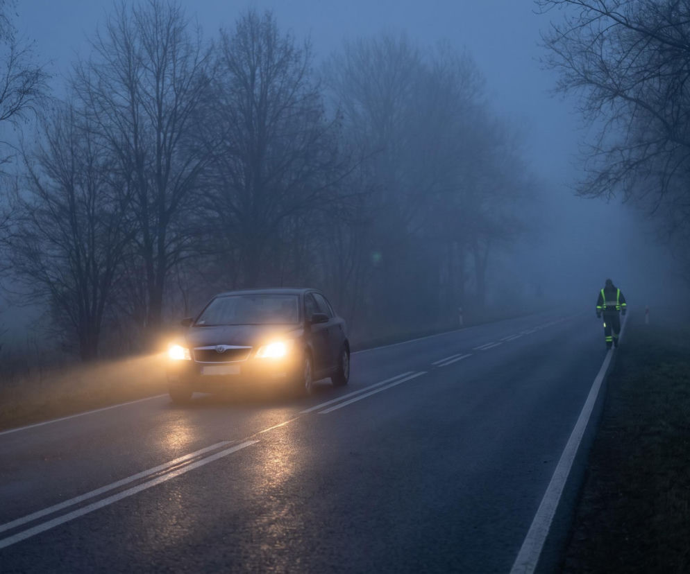 Samochód z włączonymi światłami na drodze w gęstej mgle. O ostrzeżeniach IMGW dla kierowców przeczytasz na Eska.