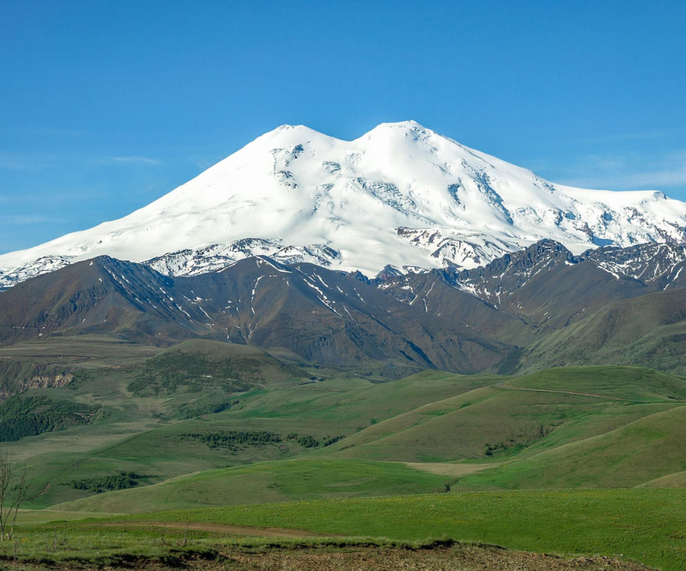 Ośnieżony szczyt Elbrusu górujący nad zielonymi dolinami. O tragedii alpinistów na tej górze przeczytasz w Eska.