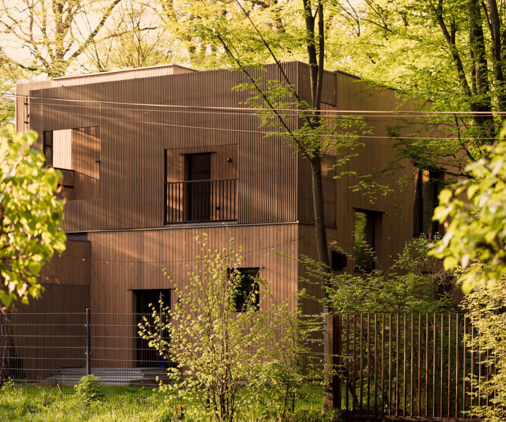 Nowoczesny dom w Podkowie Leśnej, zaprojektowany przez MFRMGR Architekci, z elewacjami z sosnowych desek, wkomponowany harmonijnie w gęsty starodrzew, otoczony zielenią. Więcej o tej realizacji na Architektura Murator Plus.
