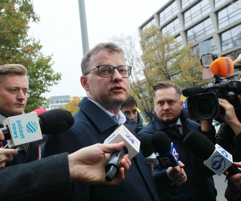 Poseł Marcin Romanowski w okularach otoczony przez dziennikarzy z mikrofonami. O sprawie aresztu przeczytasz na SE Polityka.
