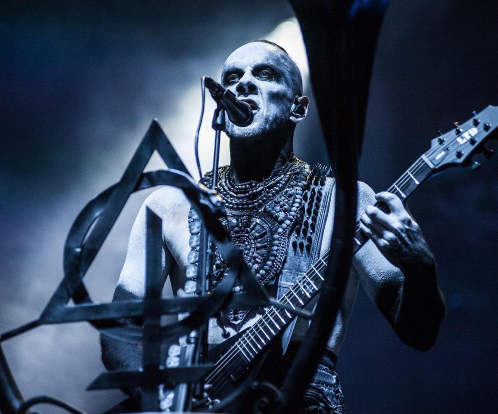 Nergal z Behemotha śpiewa do mikrofonu i gra na gitarze podczas koncertu. O planach muzyka przeczytasz na EskaRock.