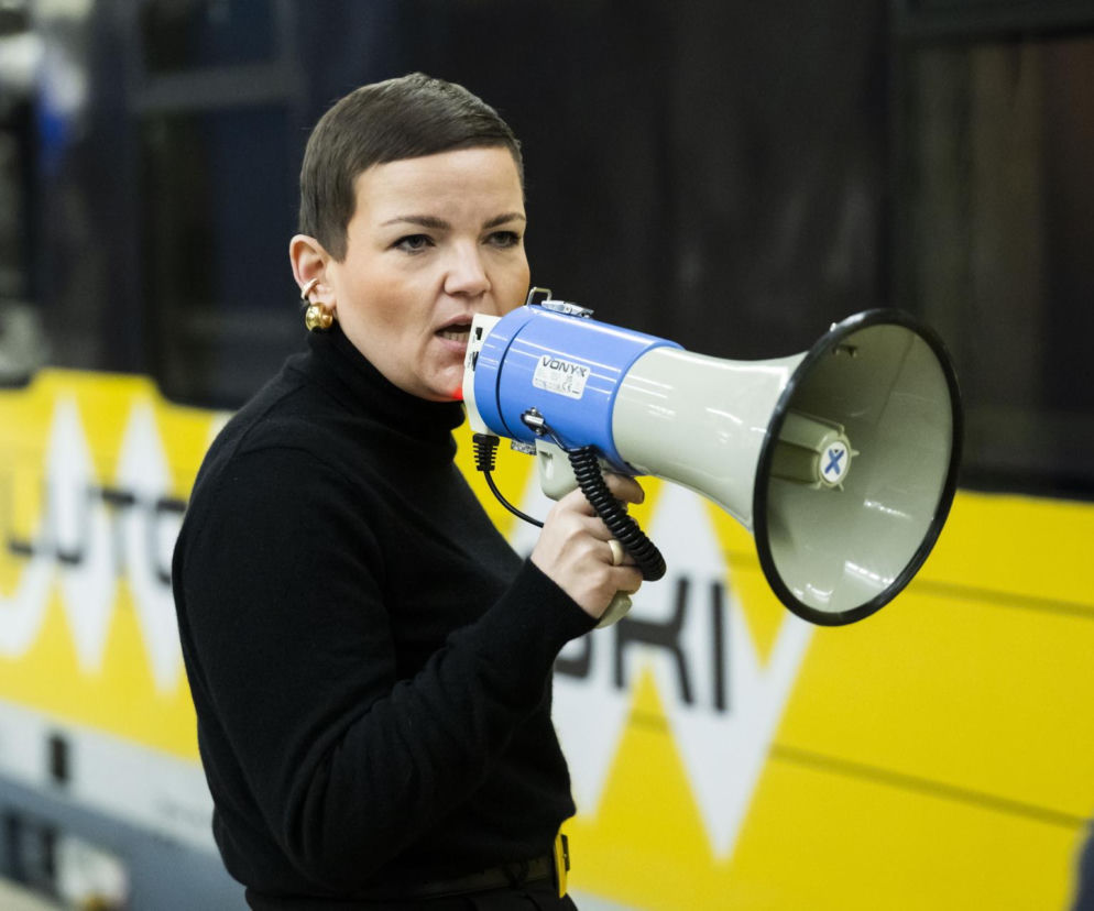 Marta Cienkowska w czarnym golfie przemawia przez niebiesko-biały megafon. O sporze o konkurs w NIAiU czytaj w Architektura.